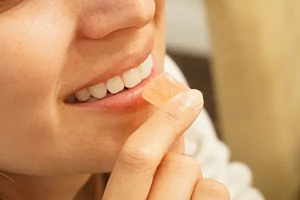 closeup of a smiling woman about to pop a cbd gummy in her mouth.