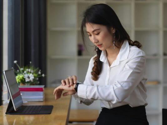 Woman checking her watch by her computer and desk